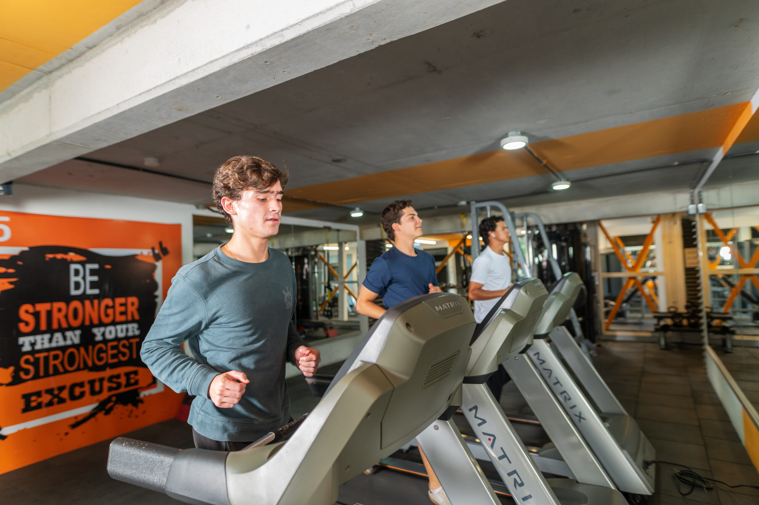 Tres jóvenes estudiantes universitarios ejercitándose en caminadoras dentro del gimnasio equipado de D15 Dorms.